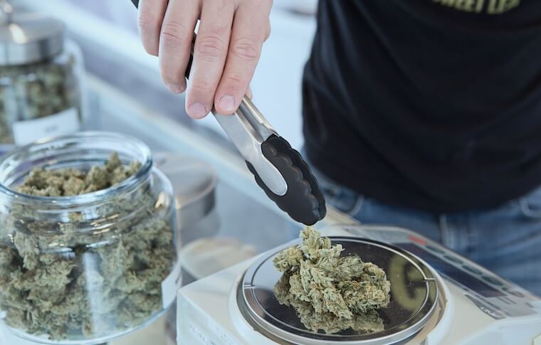 Man picking up cannabis from digital scale with tongs